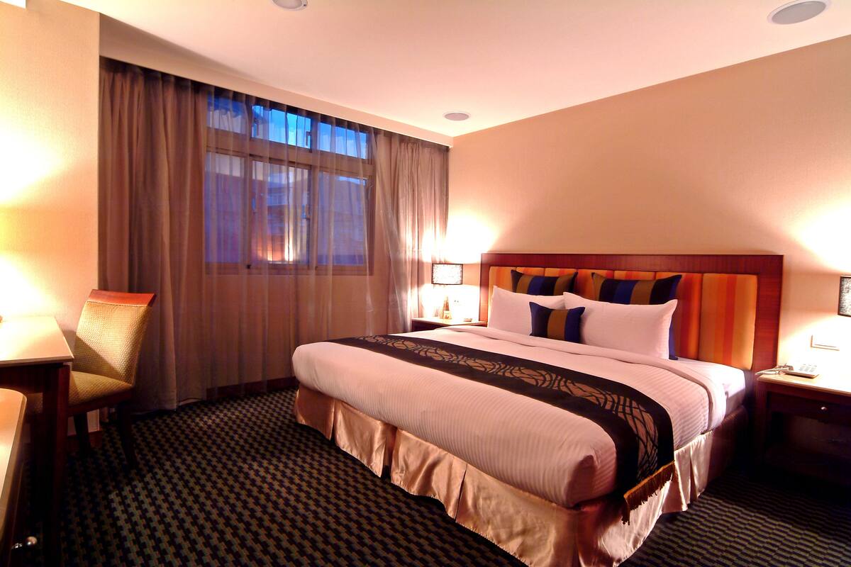A hotel room with a large bed, a chair, a desk, and a window with curtains.