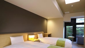 A hotel room with two beds, a small table, a lamp, and a view of greenery through the door. - Katsuragawa (Izu)