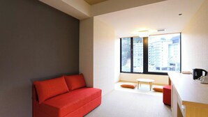 A modern room with a red sofa, a small round table, and a kitchenette area. - Katsuragawa (Izu)