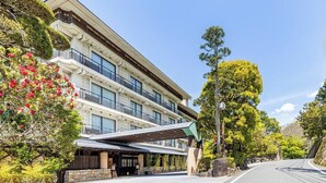 A multi-story hotel with a covered entrance, large windows, and lush greenery. - Katsuragawa (Izu)