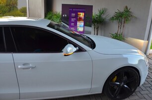 Um carro branco estacionado em frente a um prédio com uma placa.