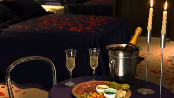 Un ambiente romántico con una cama, una mesa con champán, copas y una tabla de embutidos.