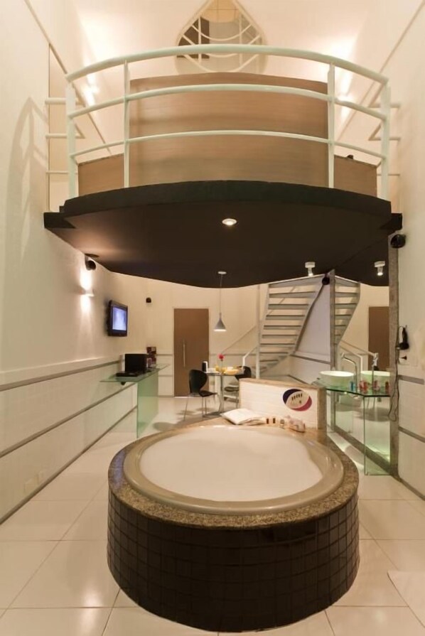 A modern bathroom with a central circular hot tub, a glass railing, and a staircase leading to an upper level. - Forum Motel (Jaboatao dos Guararapes)