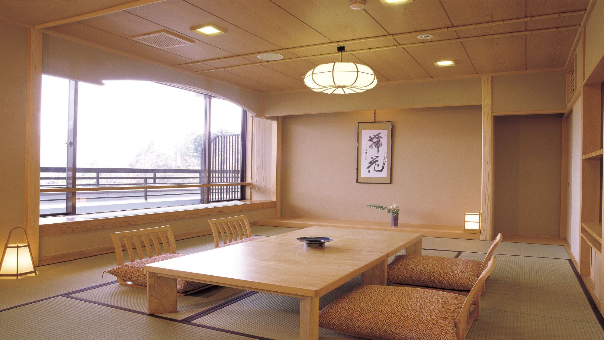 Een traditionele Japanse kamer met tatami vloerbedekking, een lage houten tafel en een uitzicht door een groot raam.