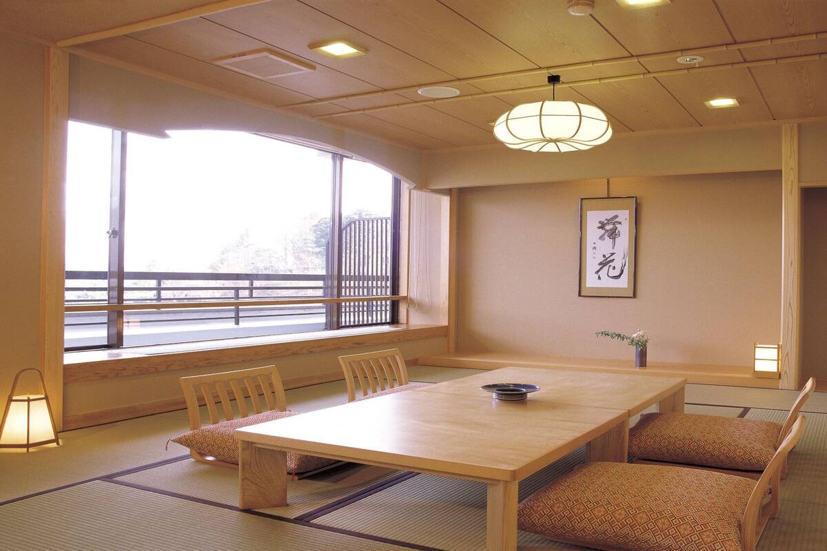 A traditional Japanese room with tatami flooring, a low wooden table, and a view through a large window.