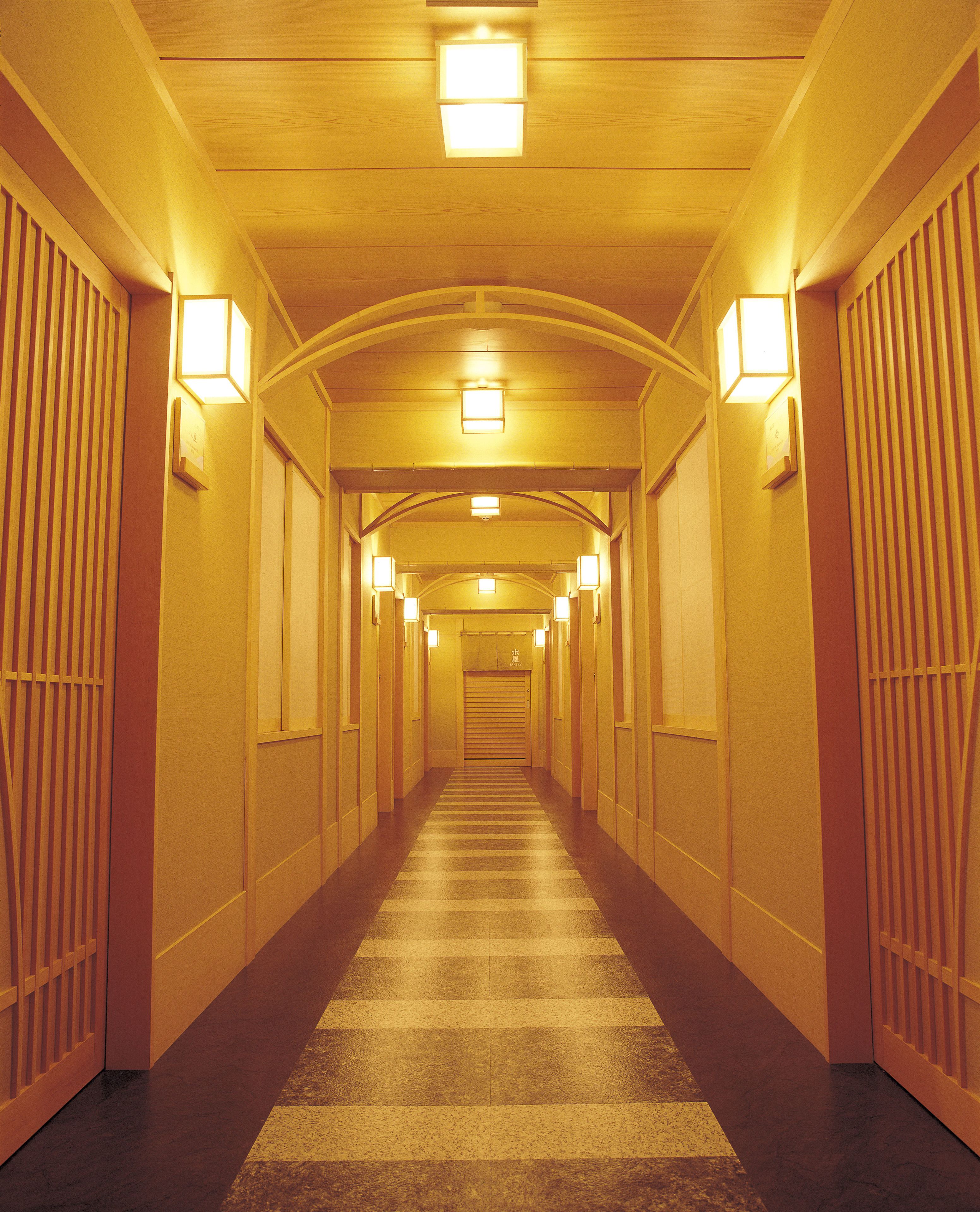 A long, narrow hallway with a striped carpet, evenly spaced lights, and wooden paneling on the walls.