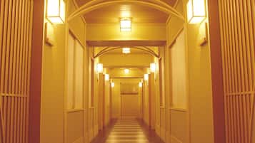 A long, narrow hallway with a striped carpet, evenly spaced lights, and wooden paneling on the walls.
