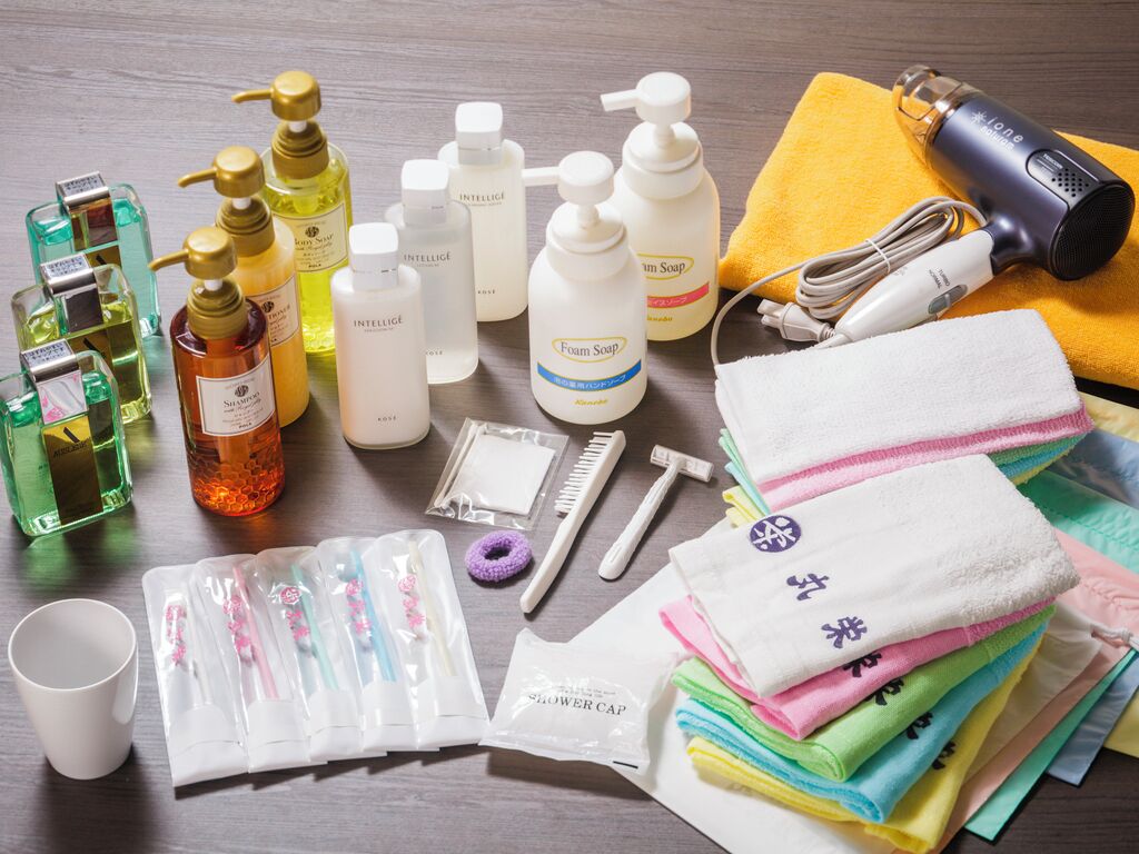 Diverse toiletartikelen en persoonlijke verzorgingsproducten, waaronder flessen shampoo, zeep en een haardroger, gerangschikt op een houten oppervlak.