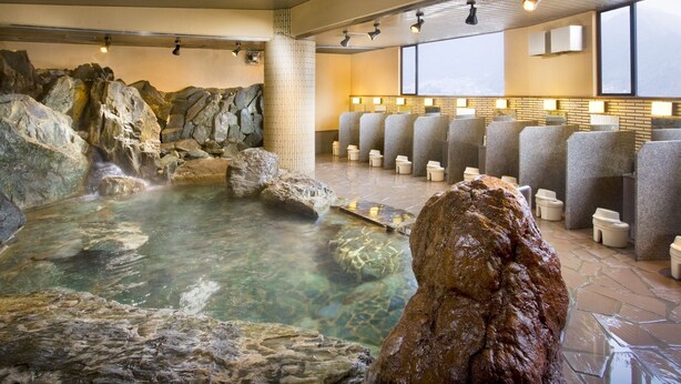 A hot spring bath area with stone walls, a clear pool, and multiple seating areas with lamps. - Wakakusa no Yado Maruei Ryokan (Fujikawaguchiko)