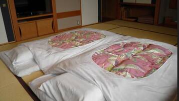 A traditional Japanese room with tatami flooring, a futon bed with a pink floral bedspread, and wooden sliding doors.