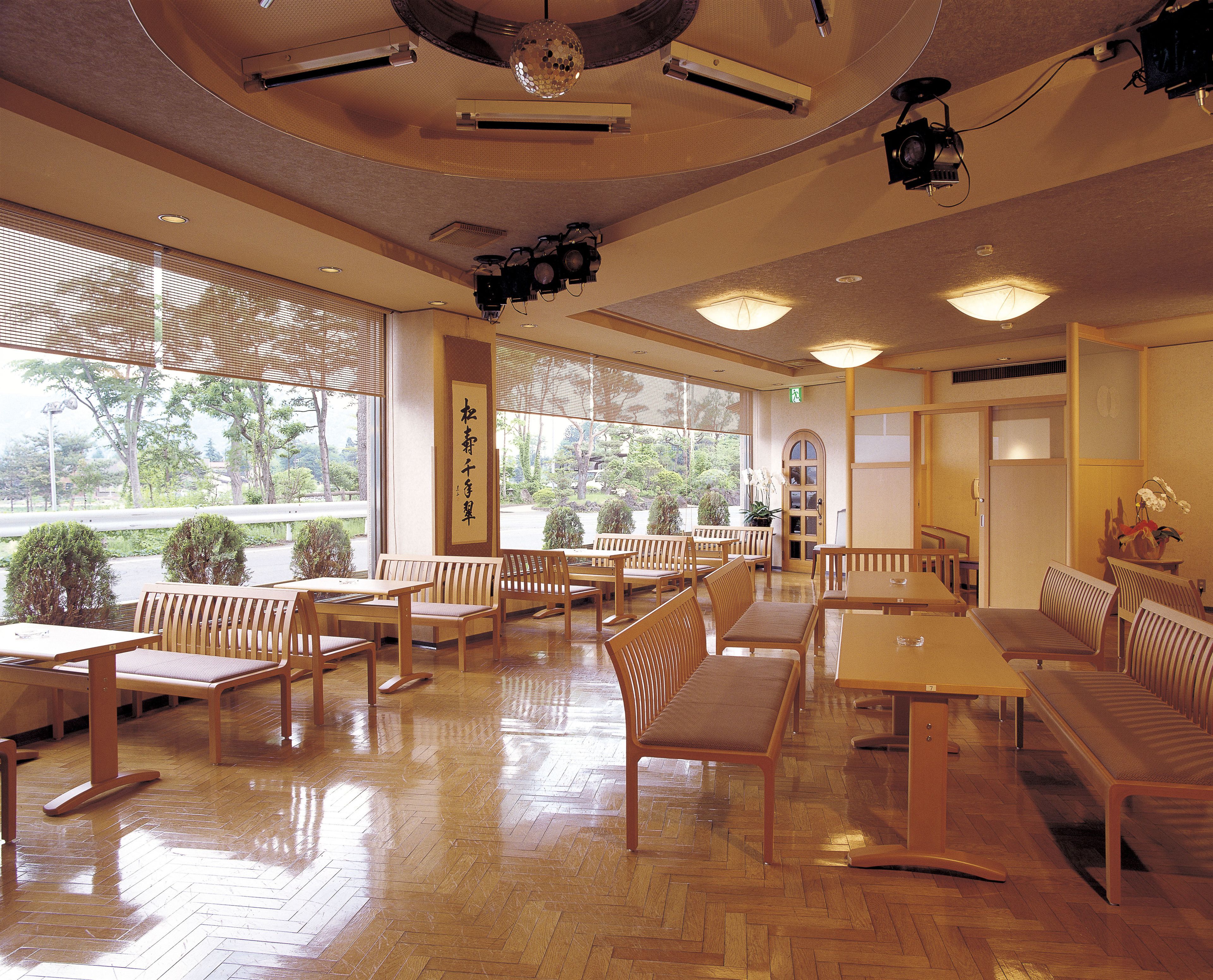 A spacious indoor area with wooden furniture, large windows, and ceiling-mounted lighting fixtures.