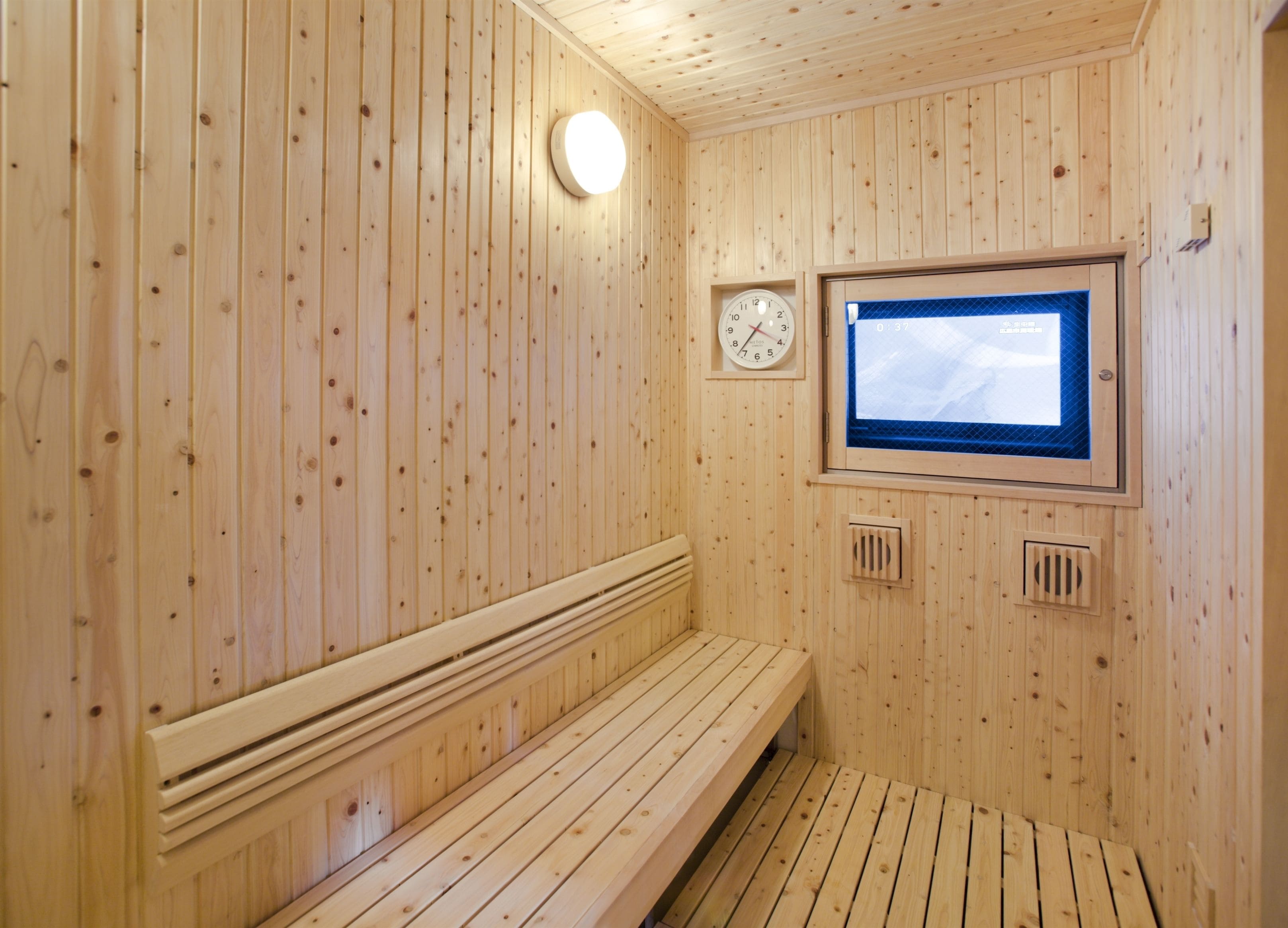 Een houten sauna met een bank, een klok en een raam.