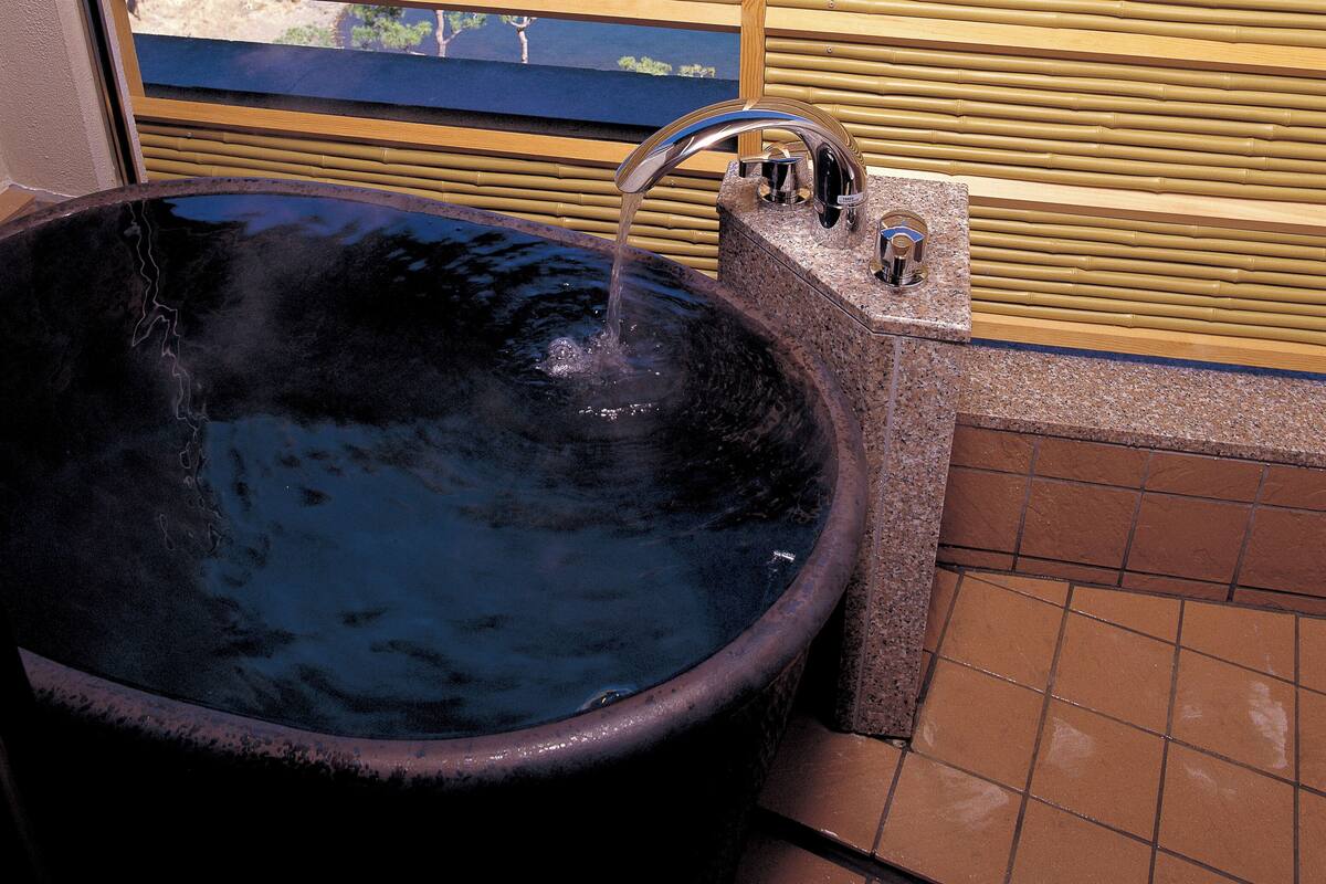 A large black bathtub with a faucet, a wooden fence, and a view of a lake and mountains.