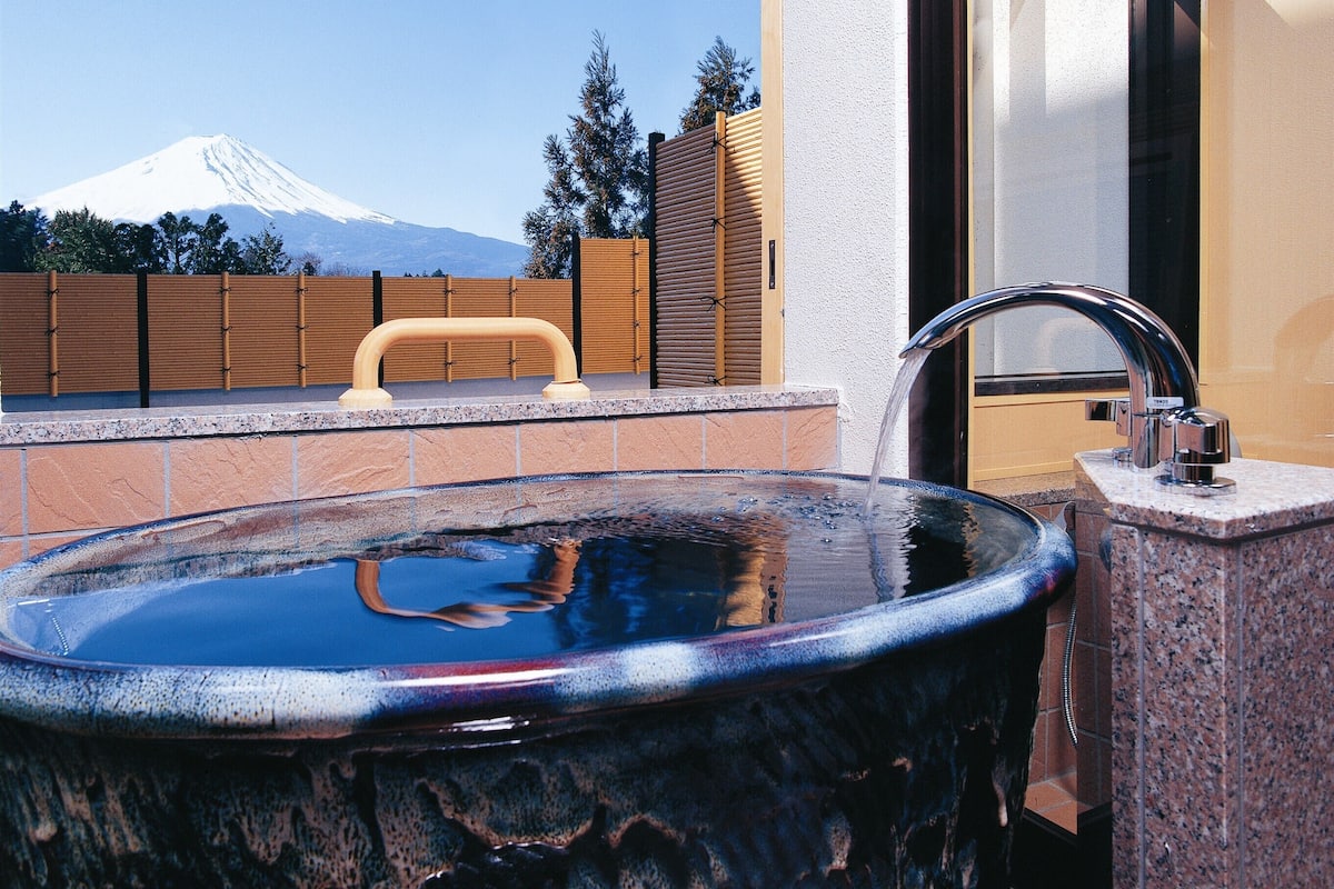 A bathroom with a large sink, a wooden fence, and a view of a mountain.