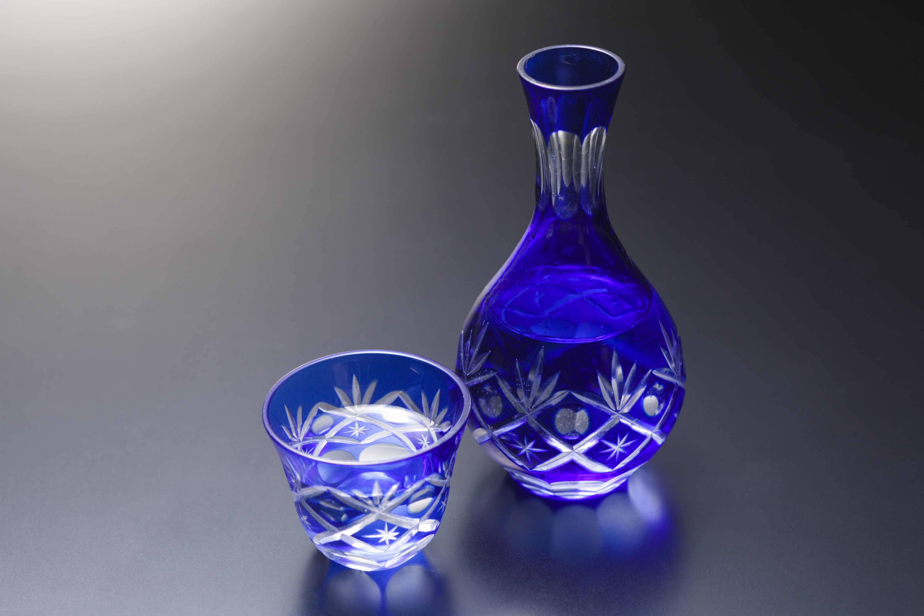 Deux vases en verre bleu ornés de motifs complexes, placés sur une surface réfléchissante.