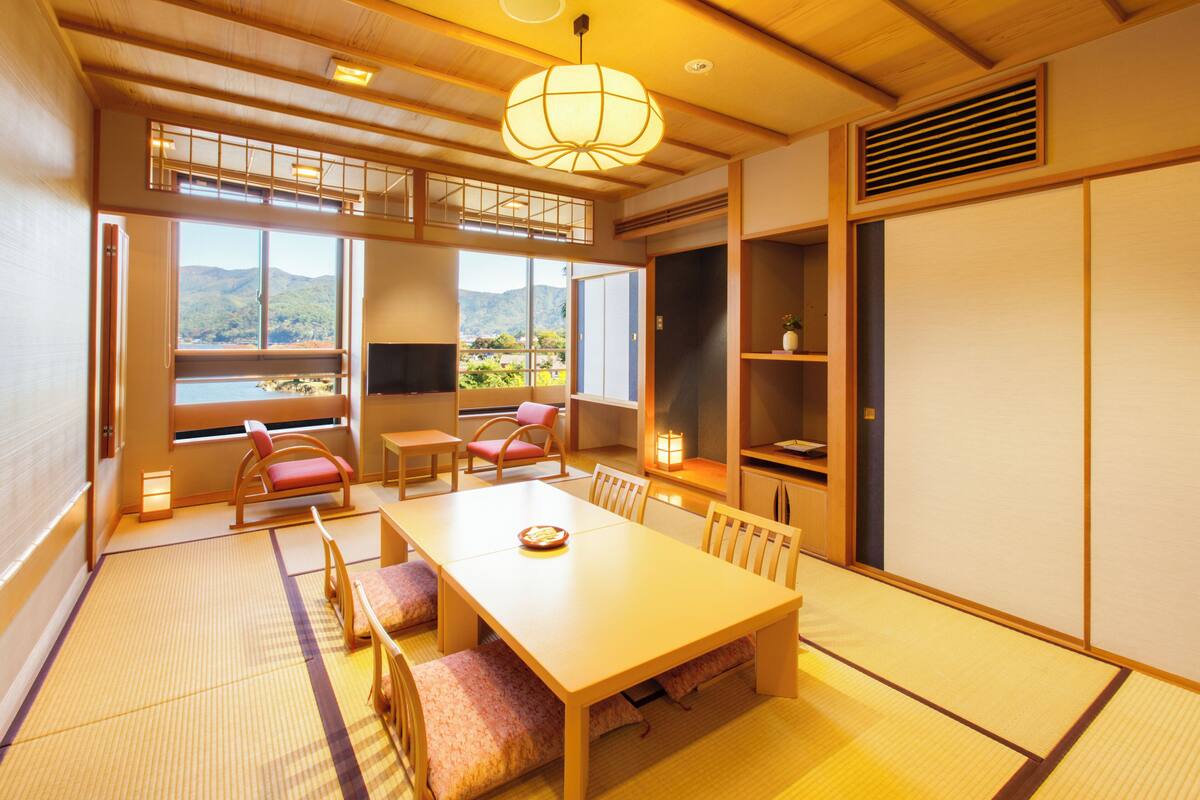 A traditional Japanese-style room with tatami flooring, a low table with cushions, and a view of mountains through large windows.