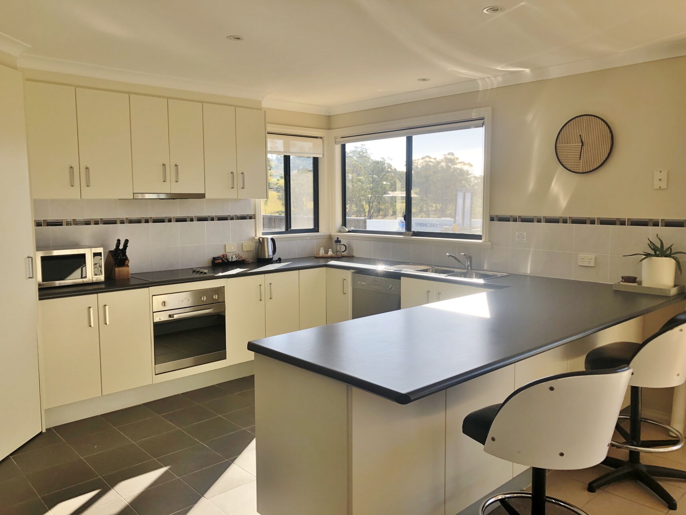 A modern kitchen with a central island, bar stools, a microwave, and a window providing natural light.