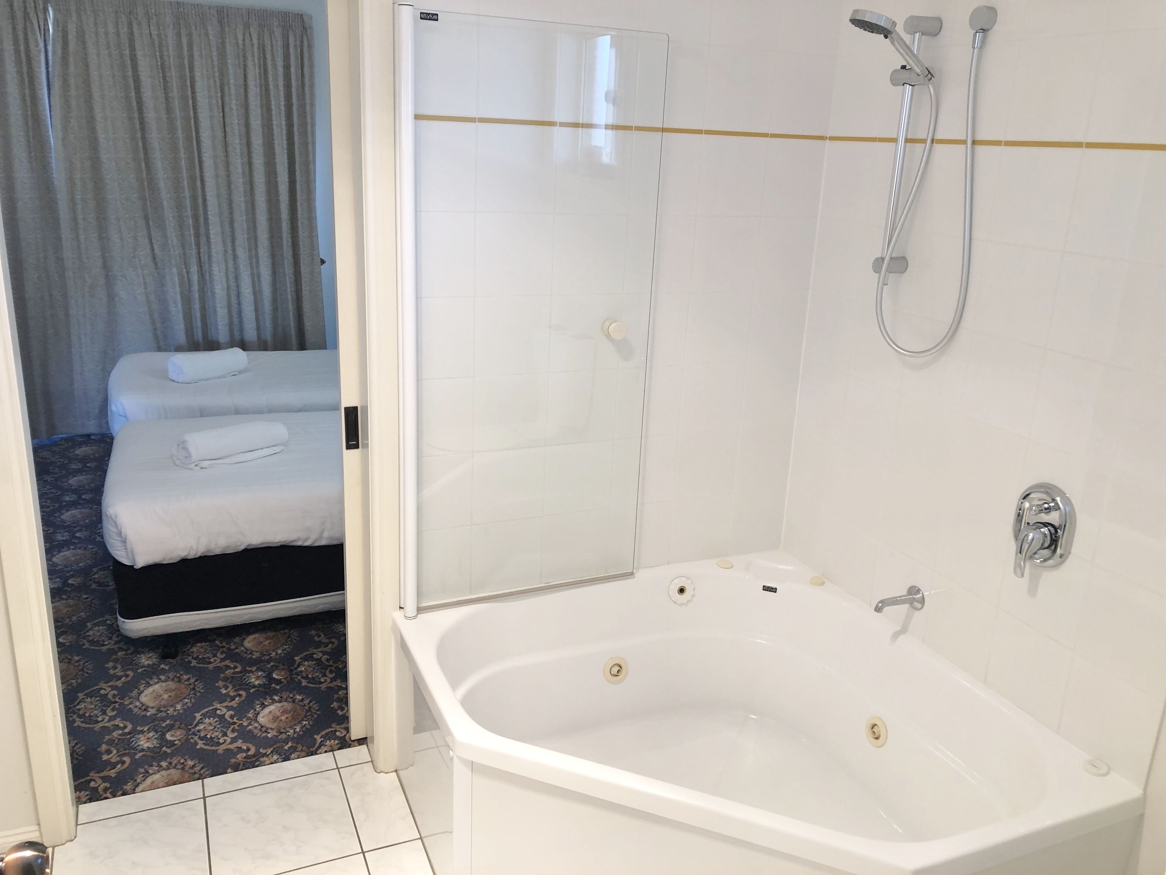 A hotel room with a large white bathtub, a shower, and two beds with white linens.