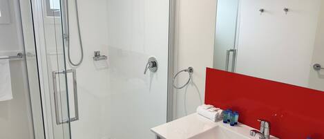 A modern bathroom with a glass-enclosed shower, a white sink with a red accent, and a large mirror.