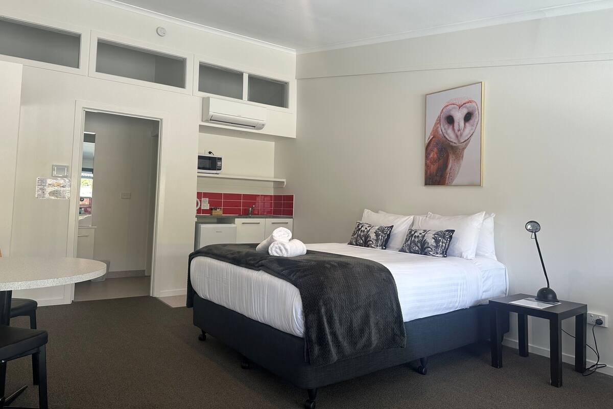 Ein Hotelzimmer mit einem Bett, einem kleinen Tisch, einem Stuhl, einem Schreibtisch, einer Mikrowelle, einer roten gefliesten Rückwand und einem Wandbild einer Eule.