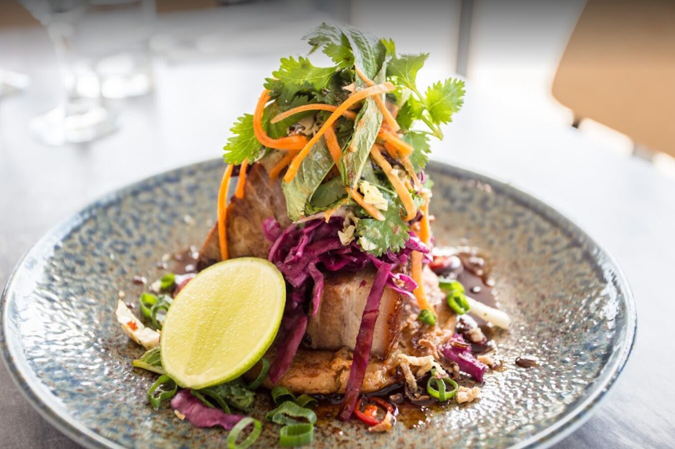 Un plat agrémenté d’un quartier de citron vert, de chou rouge et d’oignons verts, le tout présenté dans une assiette à texture particulière.