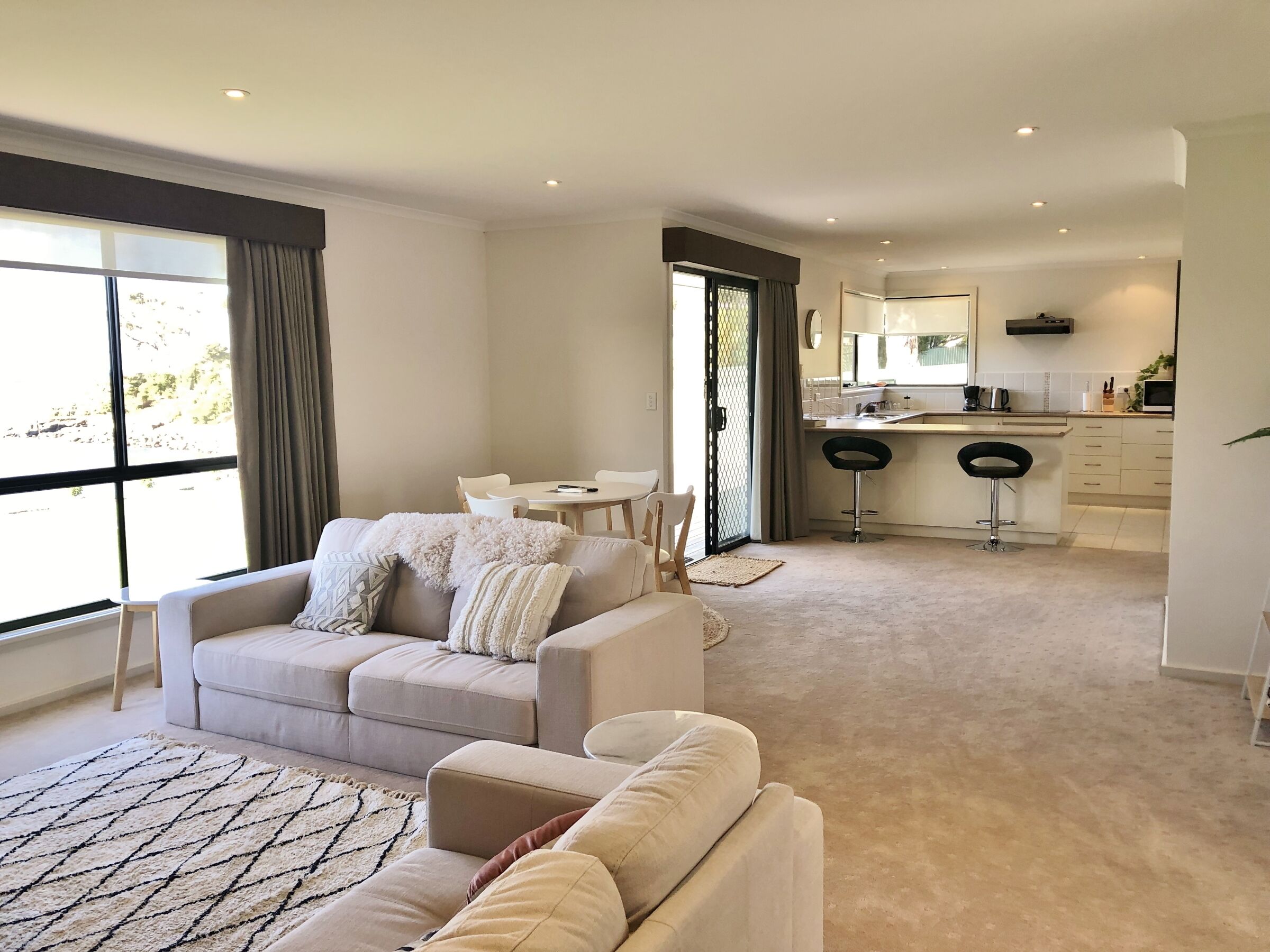 A modern living room with a beige sofa, a dining table, and a kitchen area with a bar stool.