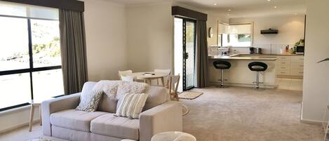 A modern living room with a beige sofa, a dining table, and a kitchen area with a bar stool.