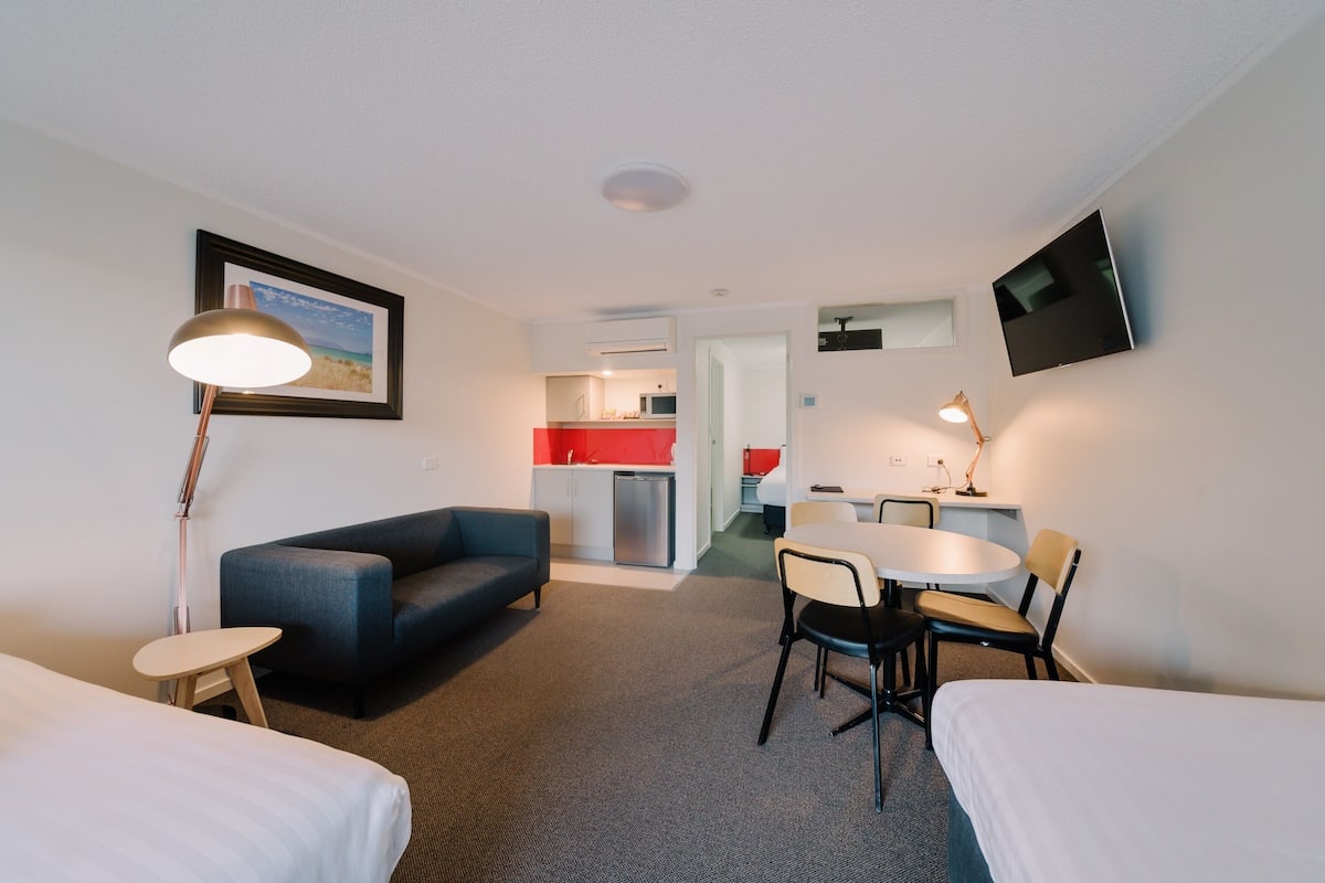 Ein Hotelzimmer mit Bett, Schreibtisch, Stuhl, Sofa, Lampe und Fernseher.