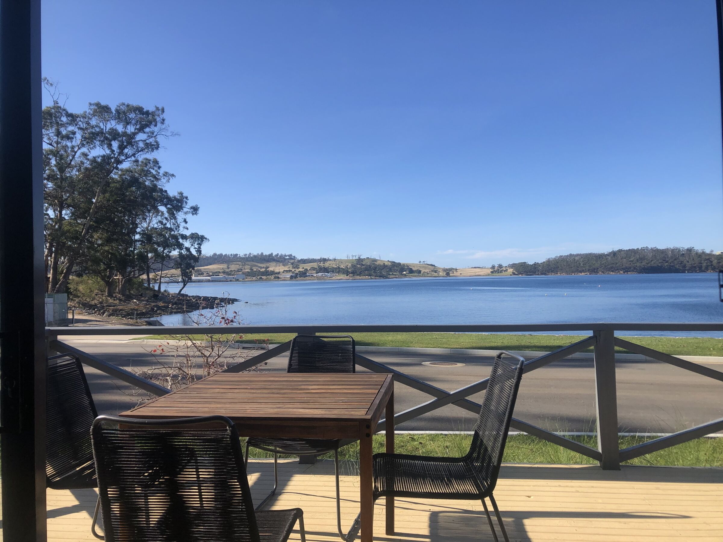 A deck with a table and chairs overlooking a lake, with a clear view of the surrounding landscape.