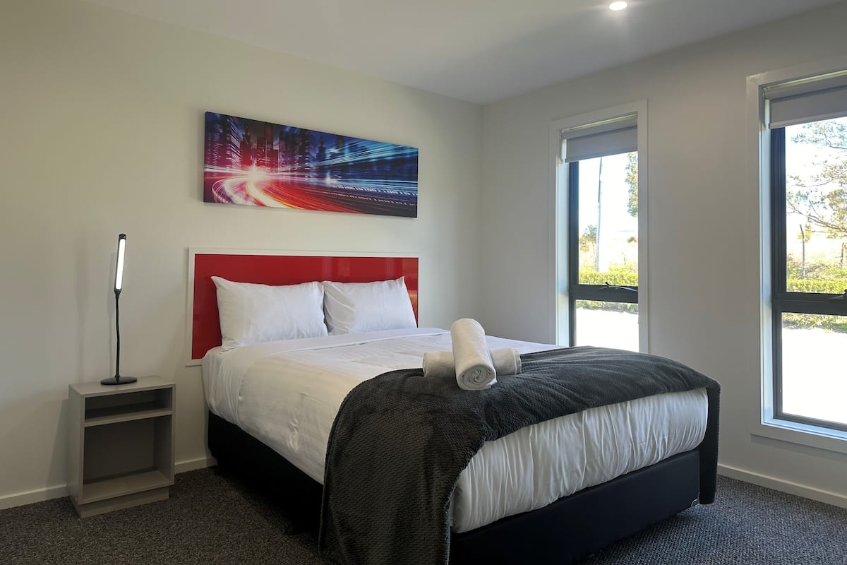 Ein modernes Hotelzimmer mit einem großen Bett, einem roten Kopfteil, einem Nachttisch, einer Stehlampe und einem Stadtbild an der Wand.