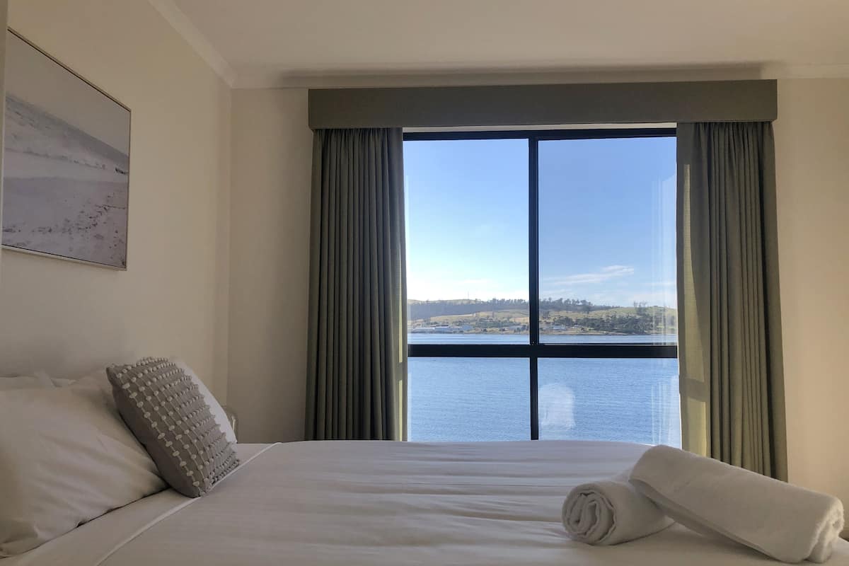 Ein Hotelzimmer mit einem großen Bett, Blick auf ein Gewässer und einem Gemälde an der Wand.