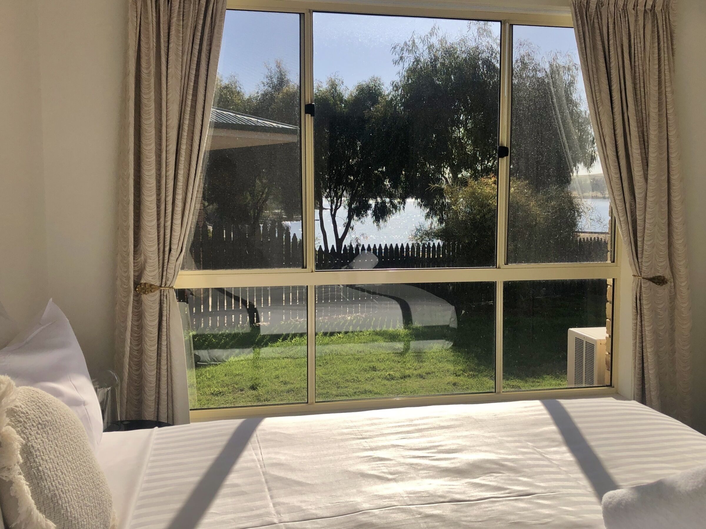 A bedroom with a large window, a bed, and a view of a grassy area and trees.