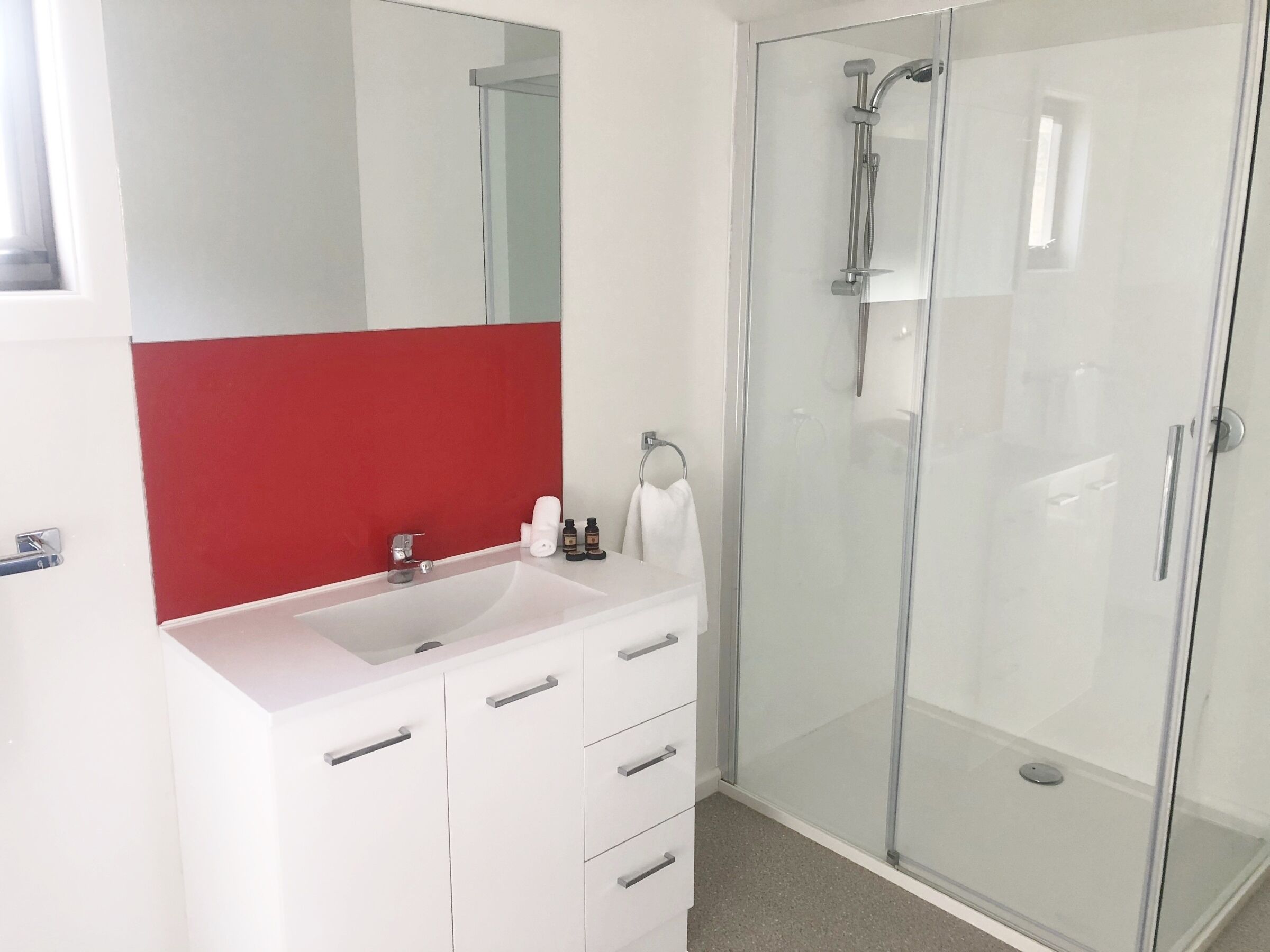 A modern bathroom with a white vanity, a glass shower enclosure, and a red accent wall.