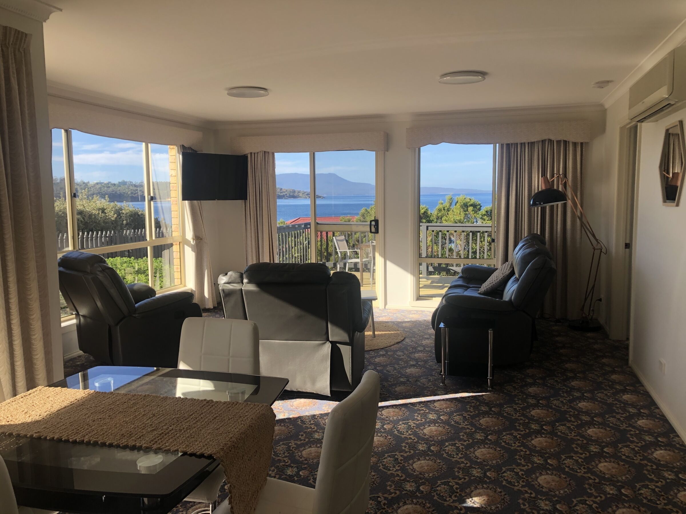 A spacious living room with a large window offering a scenic view of the sea and mountains.