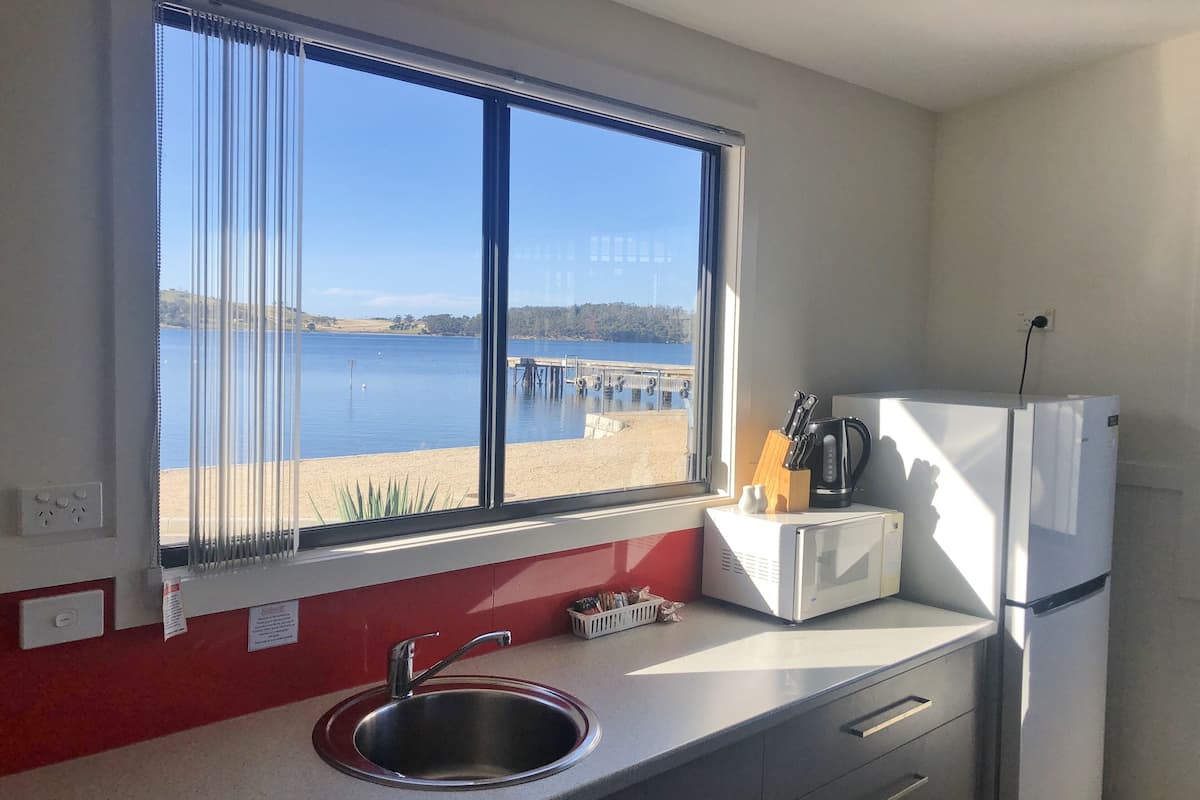 Eine Küche mit einer Edelstahl-Spüle, einem weißen Kühlschrank und einem Fenster mit Blick auf Strand und Meer.