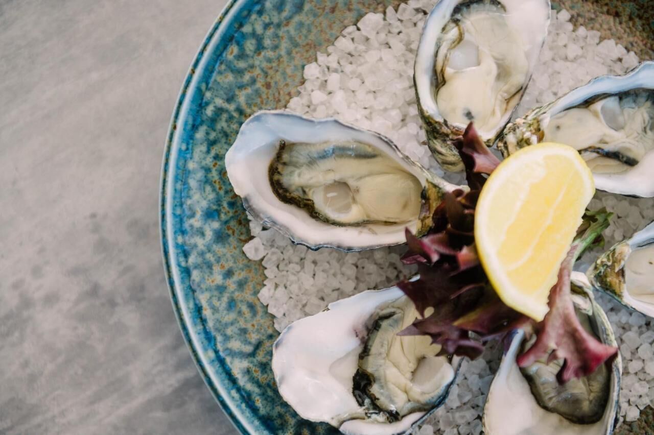 A plate of oysters with a slice of lemon and lettuce on a bed of coarse salt.
