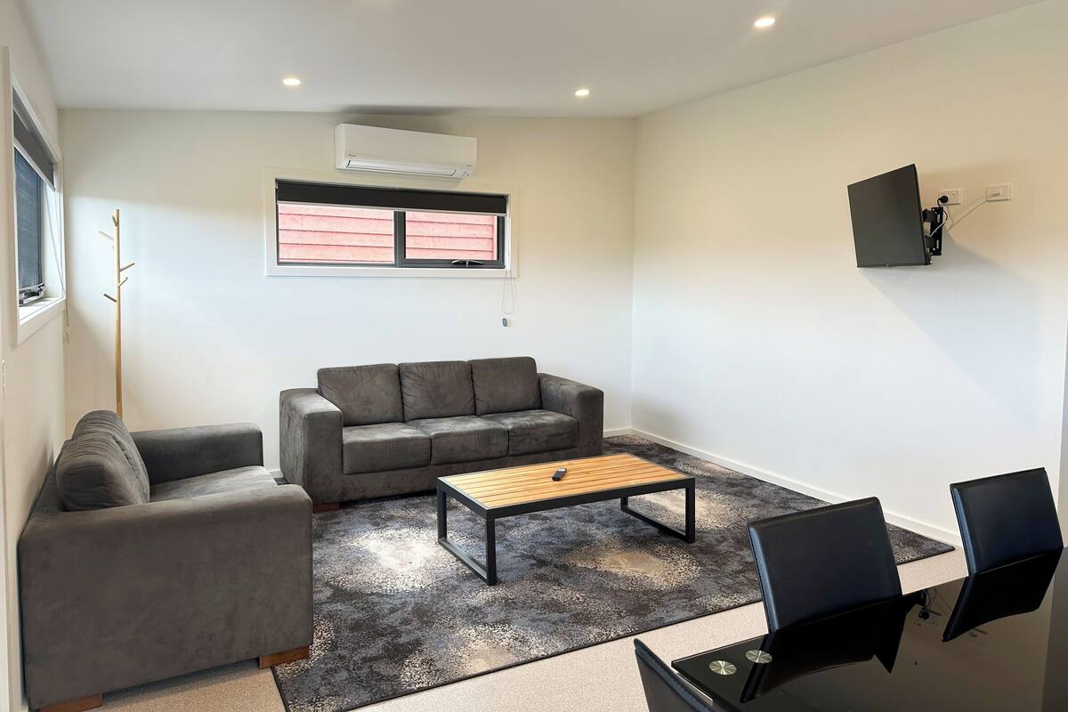 Ein modernes Wohnzimmer mit grauem Sofa, einem Holztisch und einem an der Wand befestigten Fernseher.