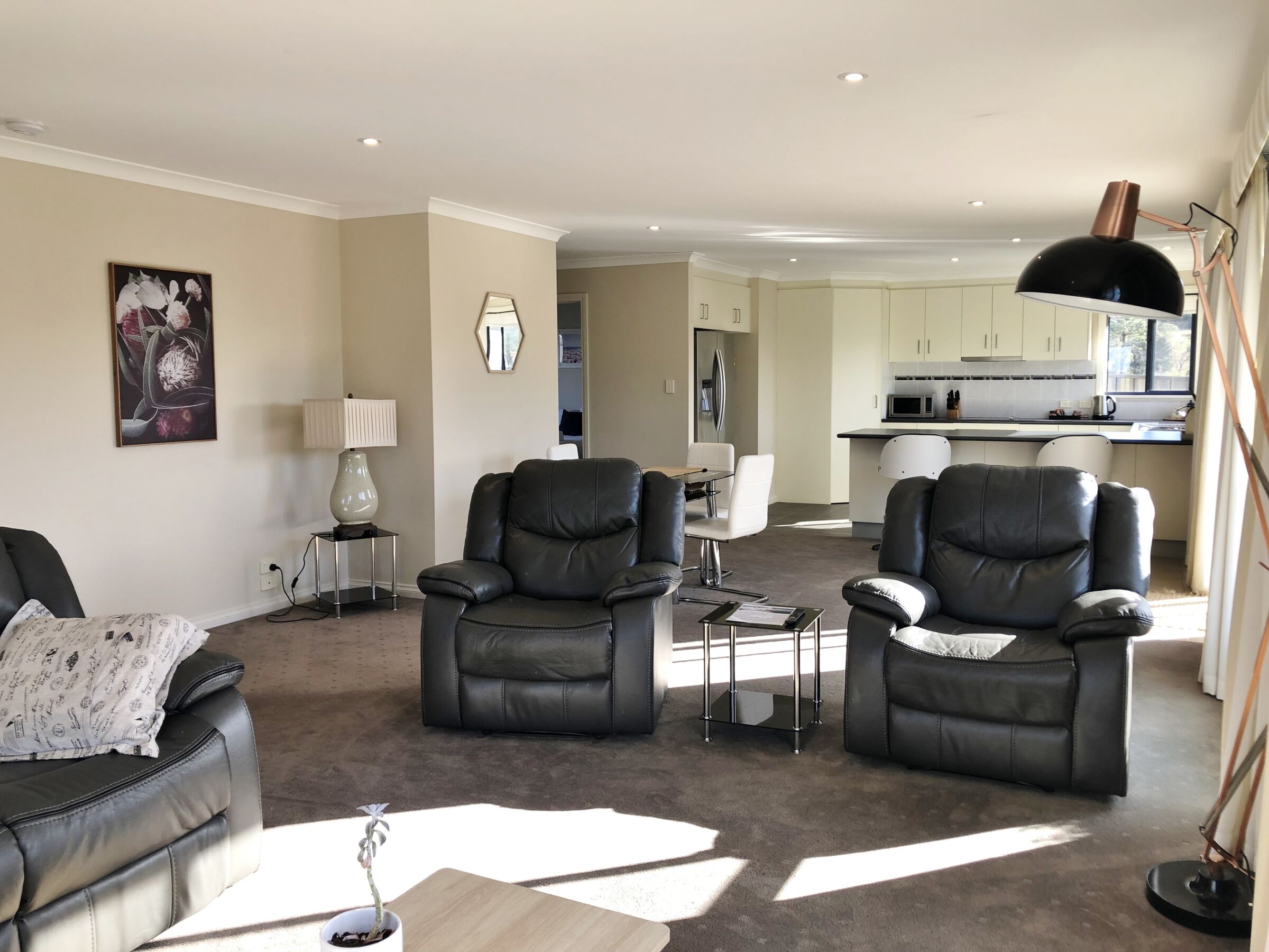 A modern living room with leather sofas, a dining table, and a kitchen in the background.