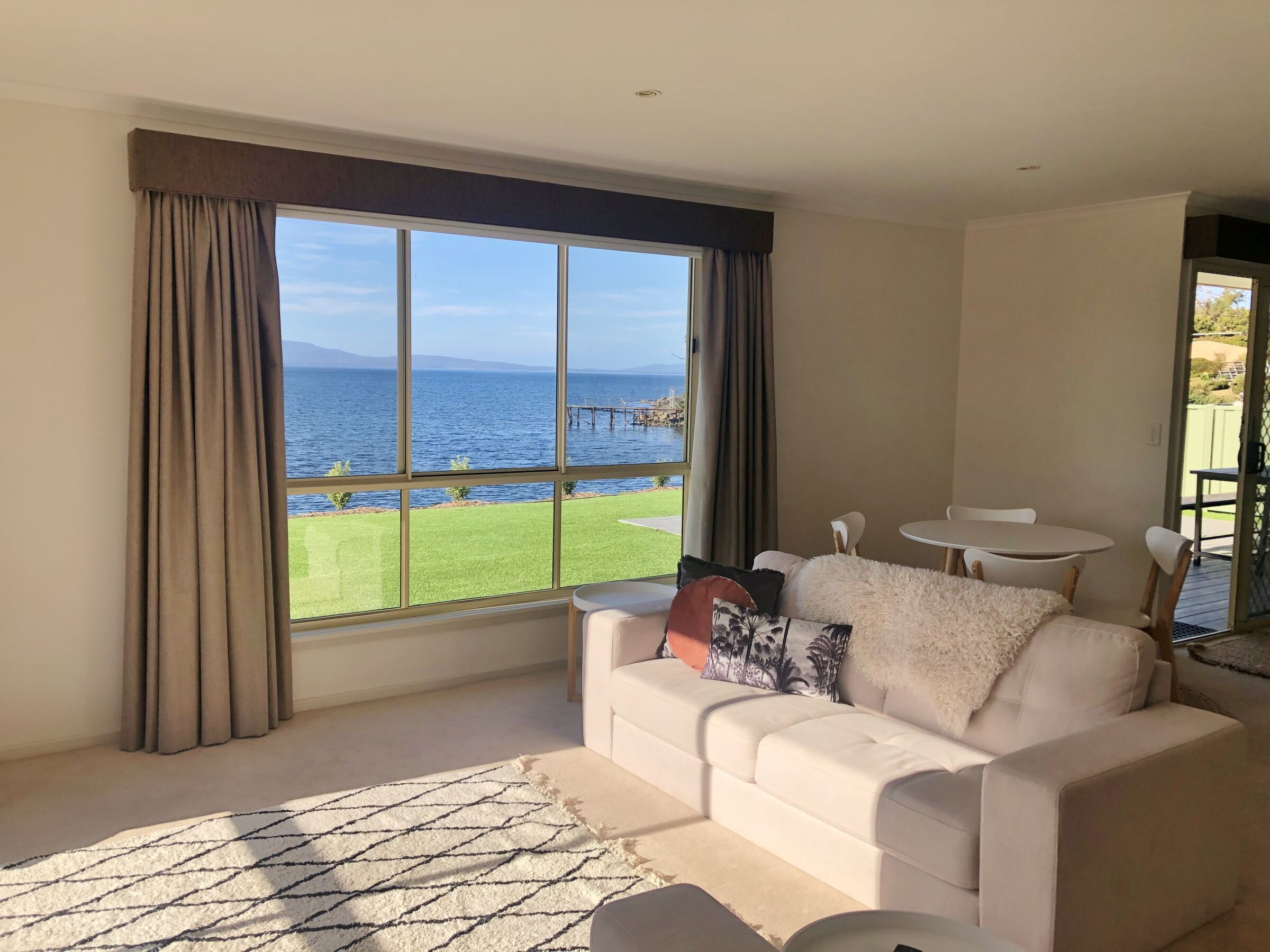 A living room with a large window, a white sofa, and a view of the sea.