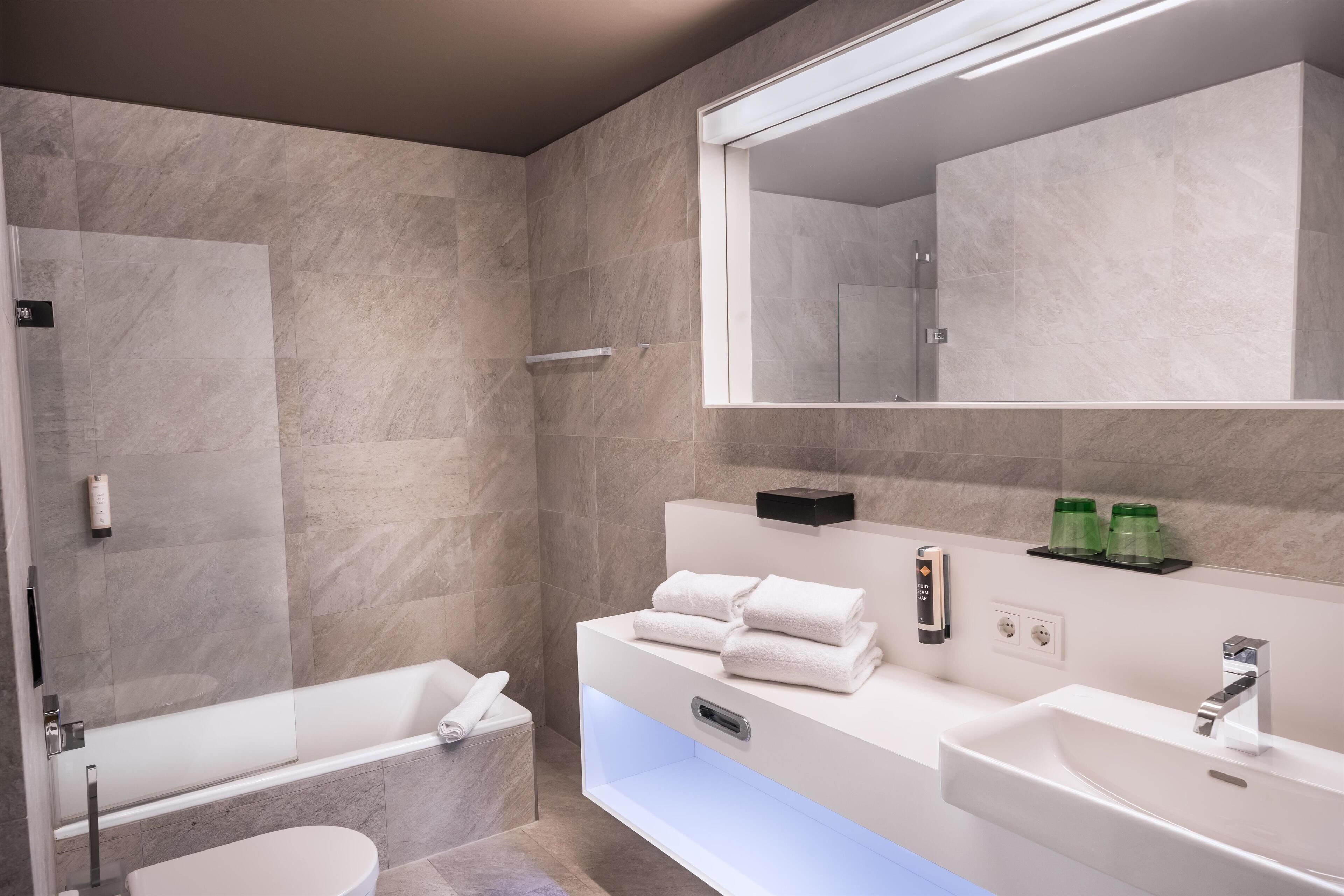 A modern bathroom with a bathtub, toilet, and vanity with a large mirror.