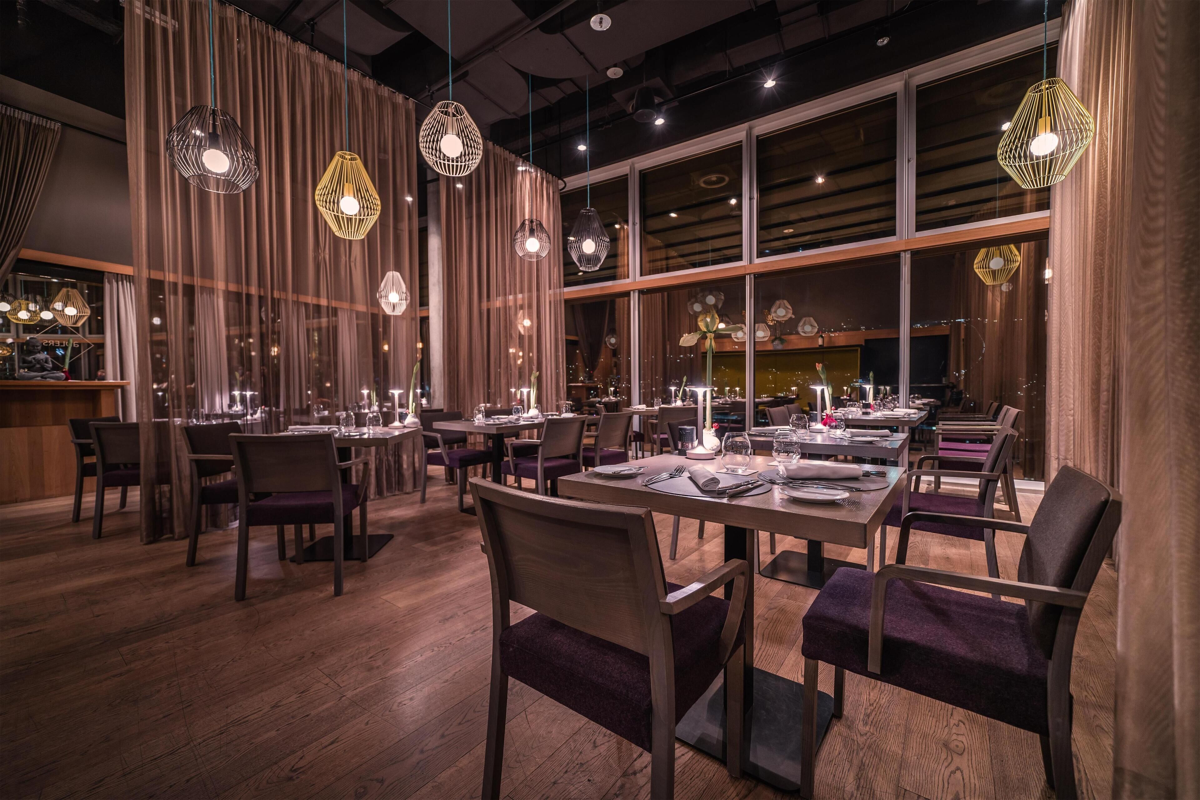 A restaurant interior with wooden flooring, tables set for dining, and hanging pendant lights.