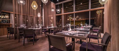 A restaurant interior with wooden flooring, tables set for dining, and hanging pendant lights.