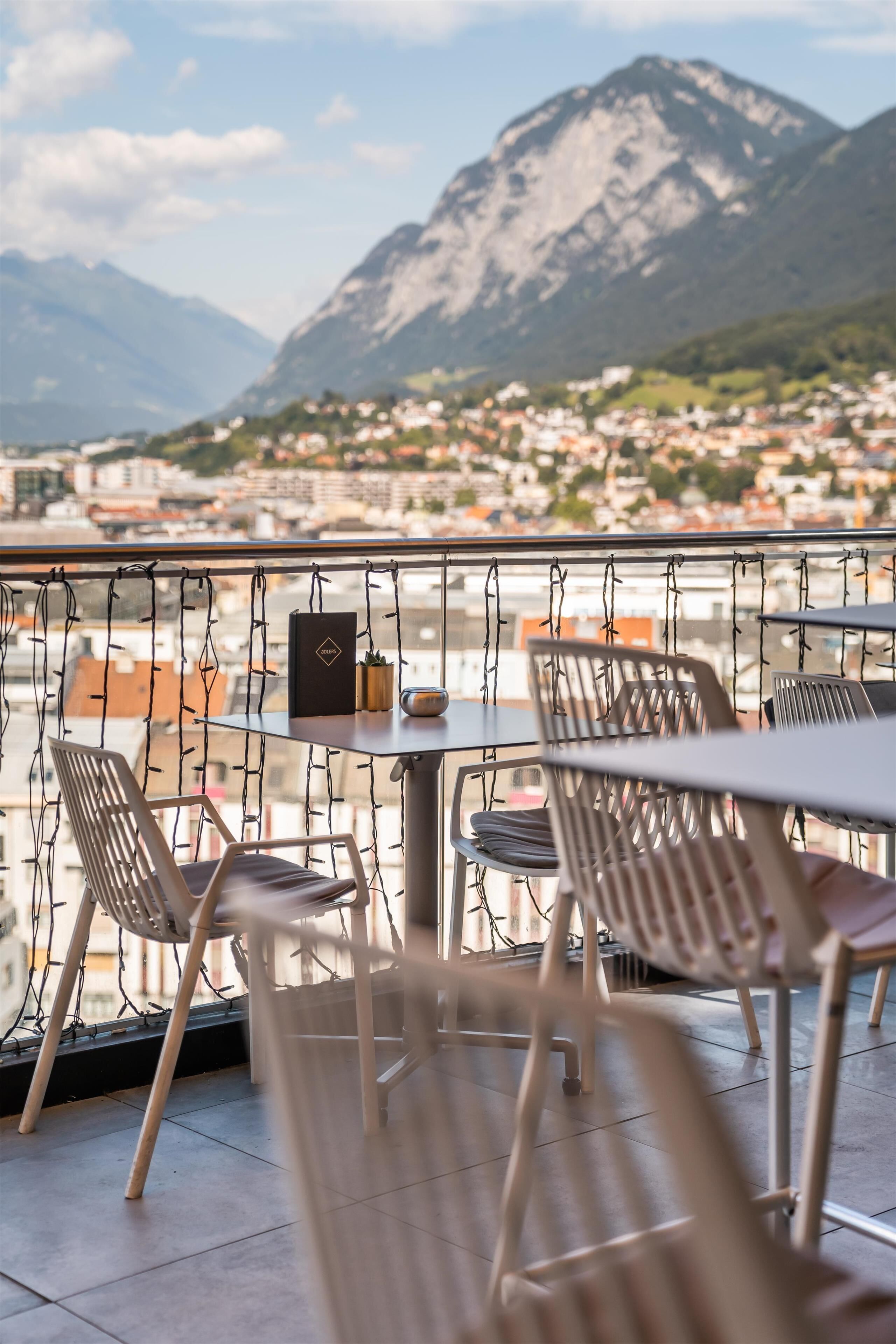 Une terrasse avec des chaises et une table, d’où l’on a vue sur une montagne et une ville.