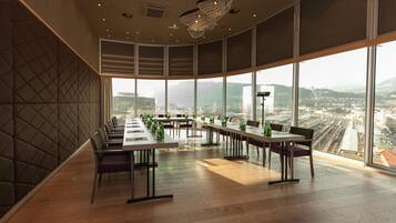 A conference room with a panoramic city view, large windows, and a modern chandelier.