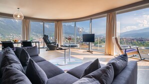 A spacious living room with a large window offering a mountain view, a comfortable sofa, a massage chair, and a flat-screen TV. - ADLERS Hotel (Innsbruck)