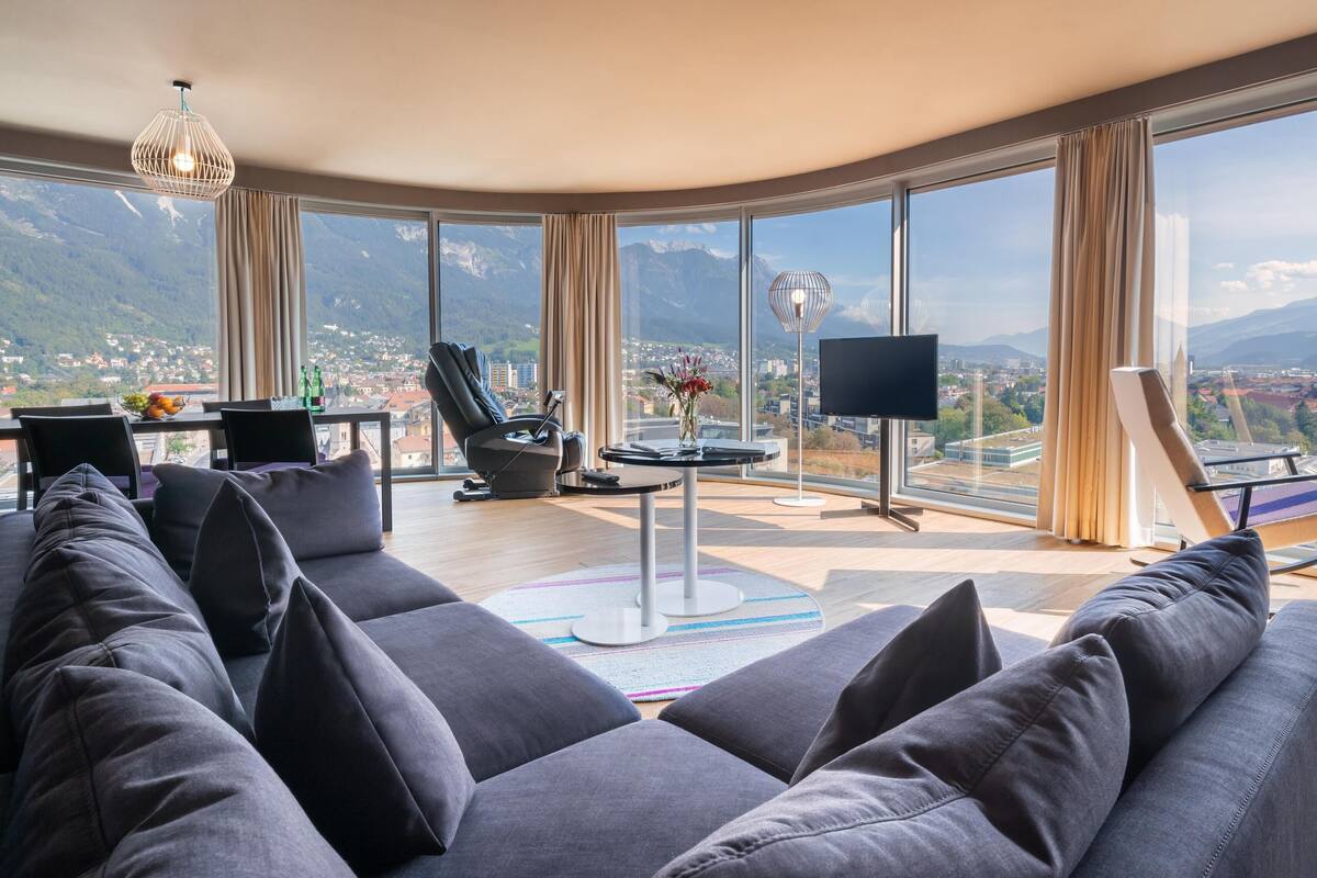 Un ampli saló amb una finestra gran que ofereix vista a les muntanyes, un sofà confortable, una cadira de massatge i una televisió de pantalla plana.
