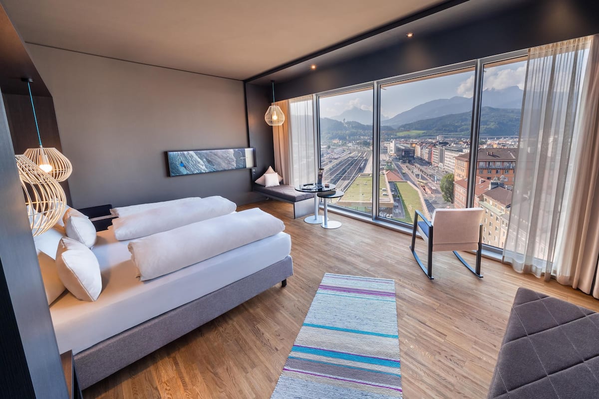 Habitació d'hotel moderna amb una finestra gran que ofereix vistes a la ciutat, un sofà, una taula petita i una cadira.