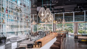 A modern bar with a long counter, shelves of bottles, and glasses. - ADLERS Hotel (Innsbruck)