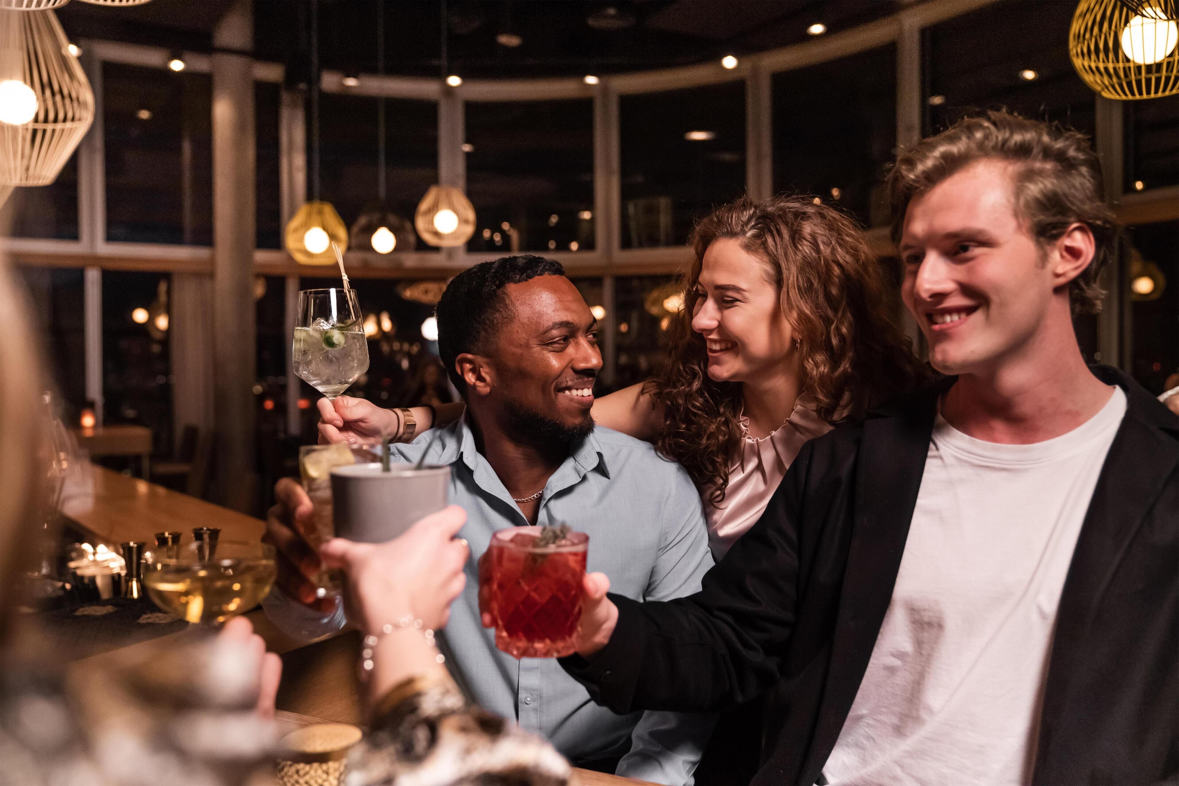A group of people at a bar with a modern interior, including pendant lighting and a large window in the background.