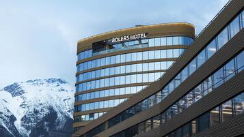 Un moderno edificio hotelero con fachada curva y grandes ventanales, que muestra el nombre 'ADLERS HOTEL'.